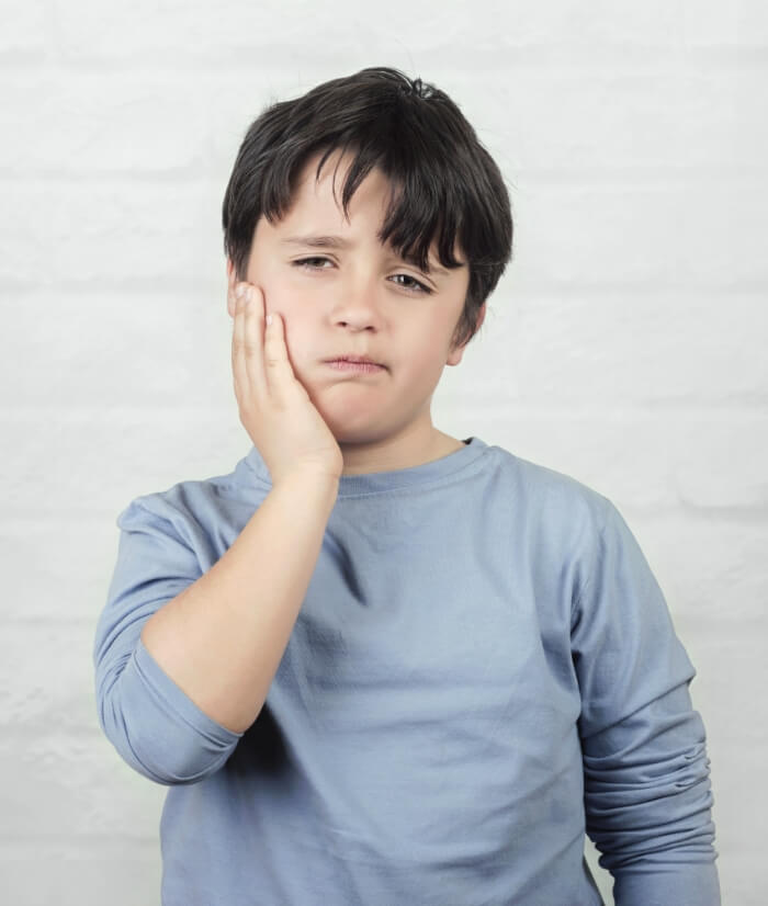 Child holding cheek in pain before emergency dentistry