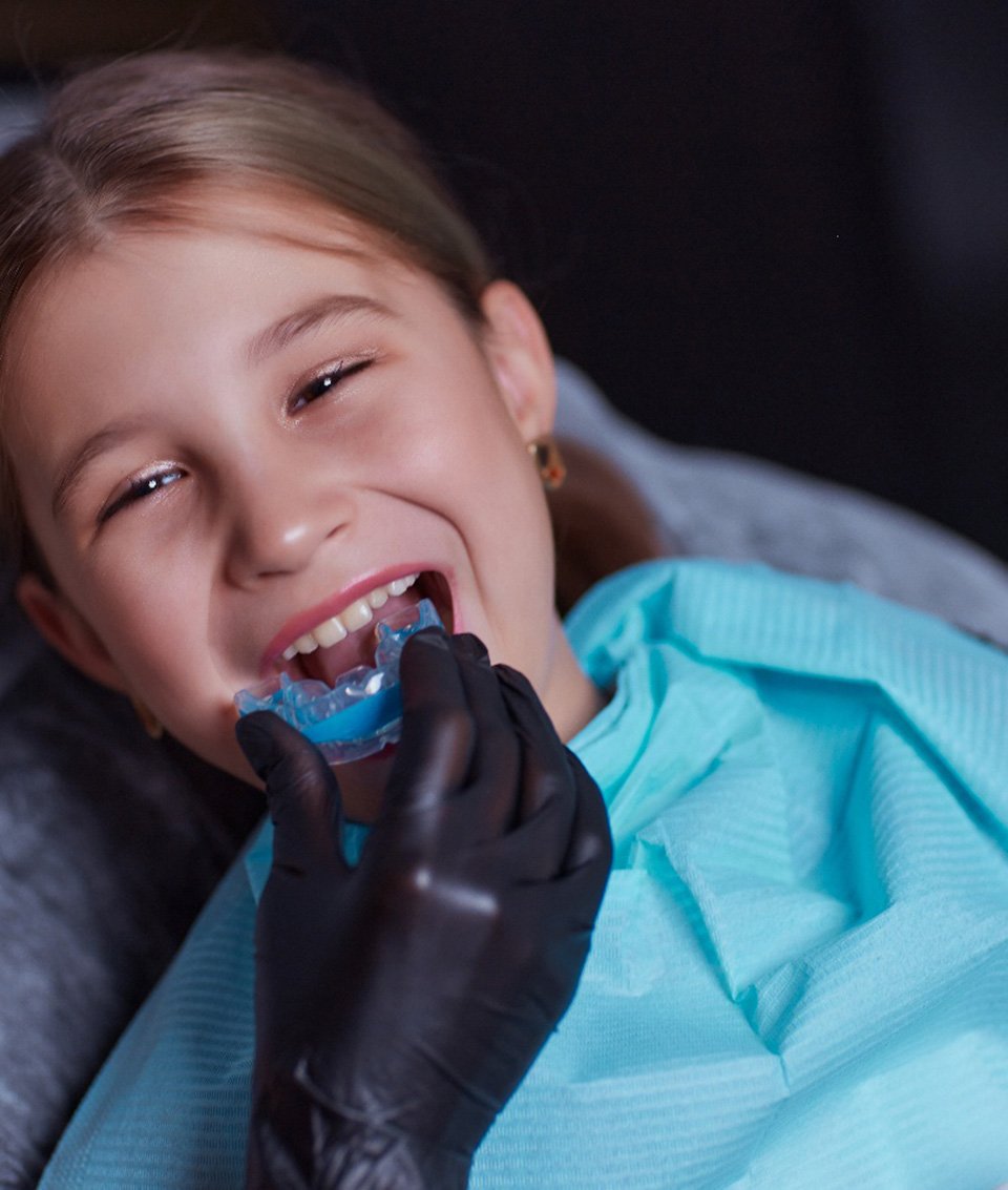 Dentist placing athletic mouthguard on smiling child