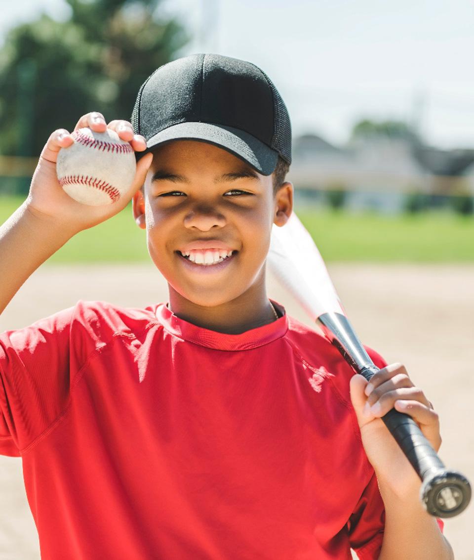 Smiling child holding baseball and baseball bat on field