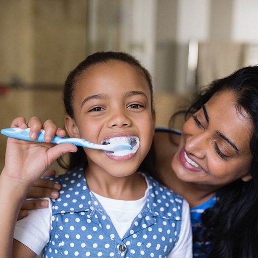 Mother helping daughter brush her teeth in the mirror