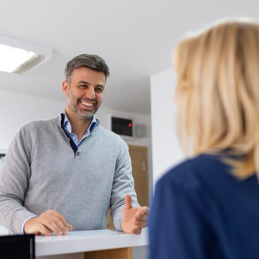 a man speaking to a front desk staff member at a dental office 