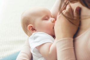 Woman in light brown sweater nursing a newborn